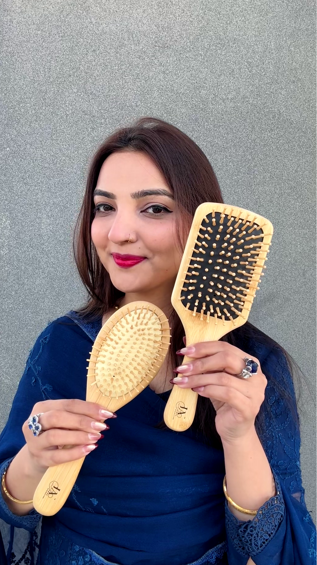 Woman holding two wooden square shape hairbrushes against a gray background