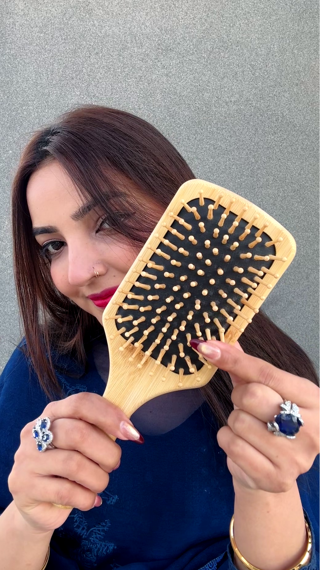 Woman holding a wooden hairbrush with black bristles against a gray background