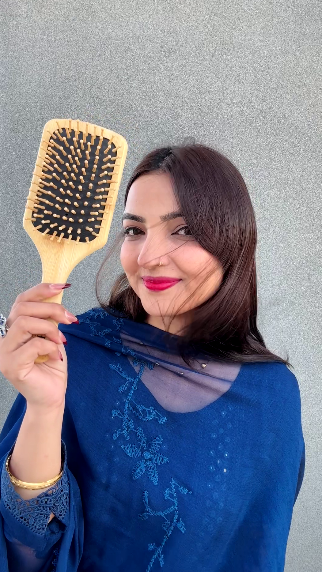Woman holding a wooden hairbrush against a gray background