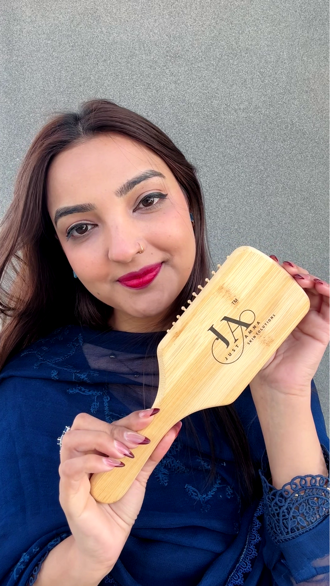 Woman holding a wooden hairbrush with a brand logo Just Amna against a gray background