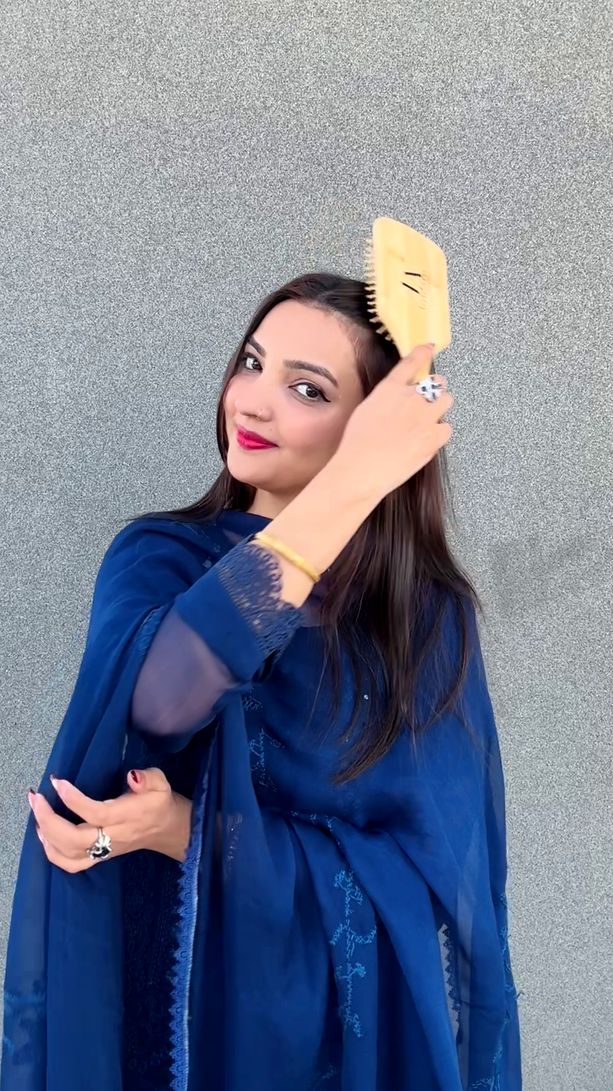 Woman in a blue dress holding a yellow hairbrush against a gray wall