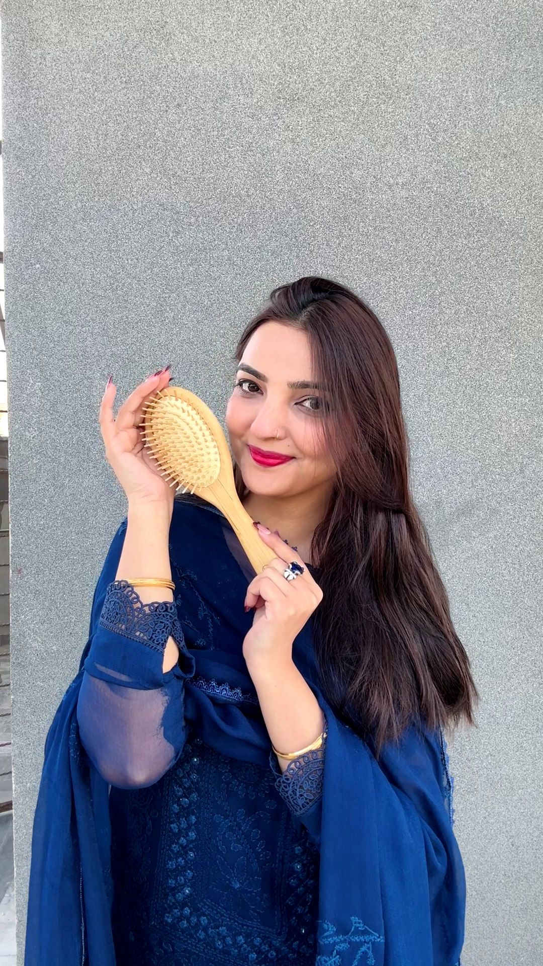Woman holding a hairbrush against a gray wall