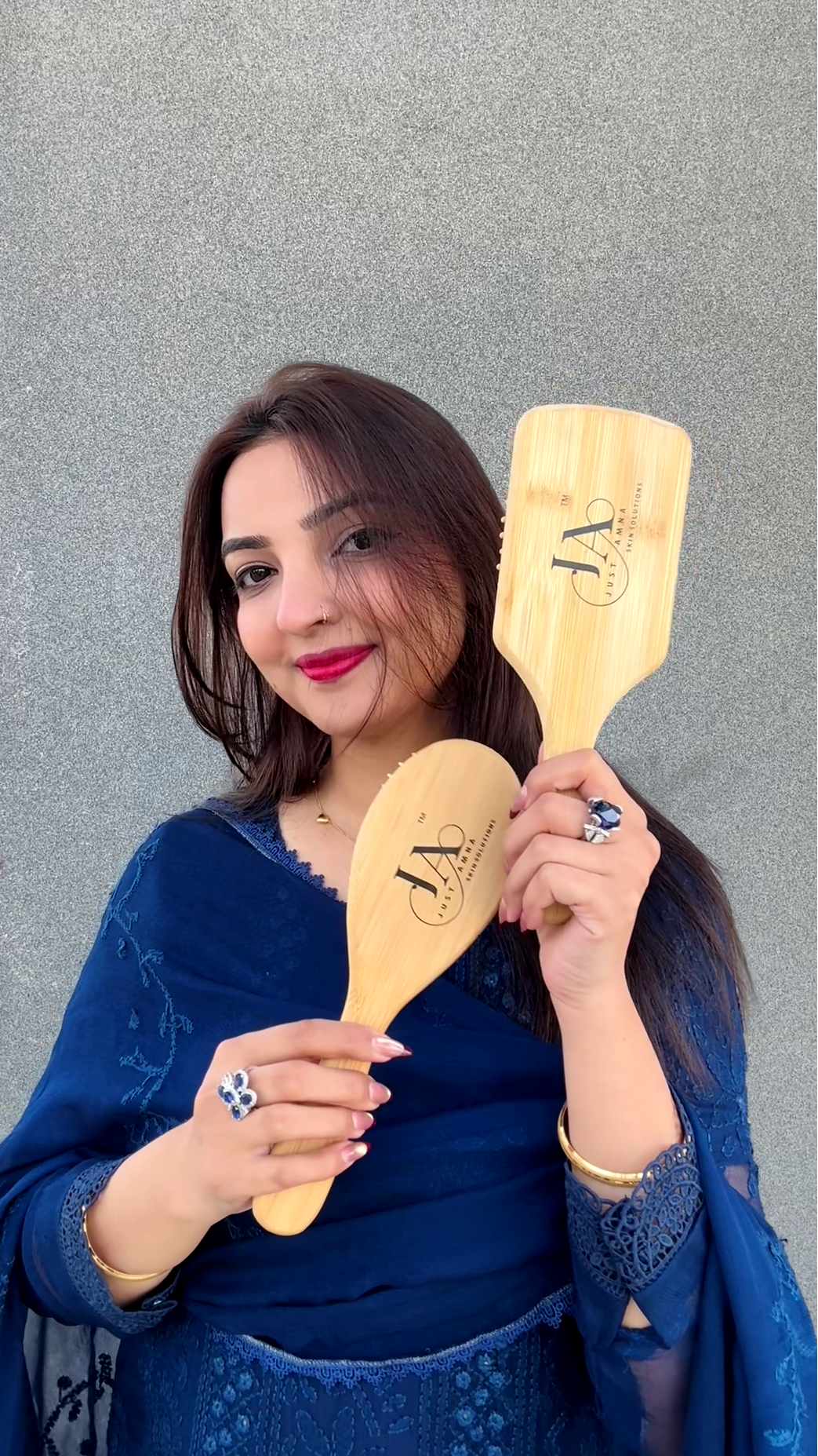 Woman holding two wooden square shape hairbrushes against a gray background
